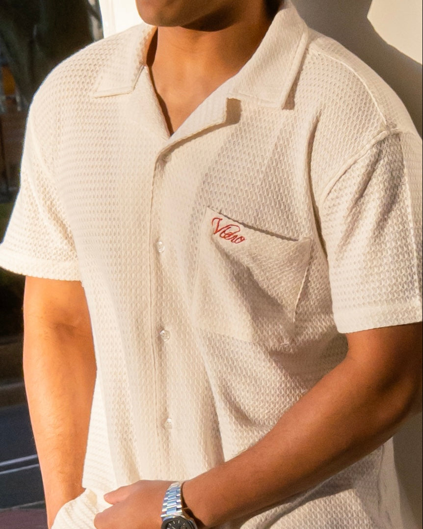 Close-up of a person wearing a textured beige shirt with a logo, standing against a blurred background.